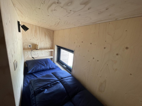 Pequeño dormitorio moderno con cama individual y ropa azul en Tiny House Plus en De Rijp, Países Bajos.