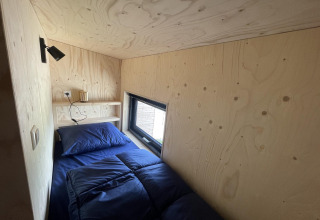 Kleine, moderne slaapkamer met eenpersoonsbed en blauwe dekens in Tiny House Plus te De Rijp.