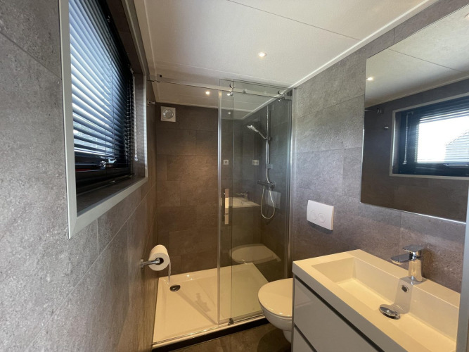 Modern bathroom at Tiny House Plus, De Rijp, Netherlands, featuring a shower, toilet, and sink unit.