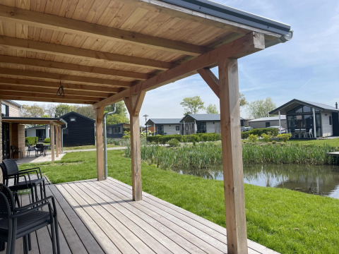 Vista desde la terraza de madera del Tiny House Plus en De Rijp, Países Bajos, con estanque y cabañas.