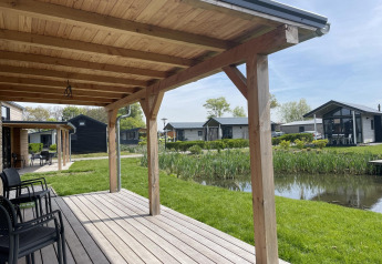 Uitzicht vanop het houten terras van de Tiny House Plus lodge in De Rijp, Nederland, met vijver en huisjes.