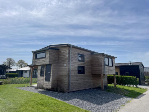 Casa pequeña de madera Tiny House Plus en De Rijp, Países Bajos, rodeada de césped bajo un cielo azul claro.