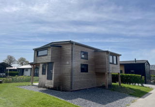 Het eigentijdse Tiny House Plus in hout bij De Rijp, Nederland, met gras en heldere blauwe lucht.