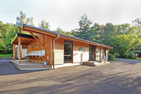 Edificio de madera con zona de fregaderos exteriores en Huttopia Royat, parque vacacional en Auvergne-Rhône-Alpes, Francia.