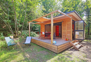 Houten chalet met terras en tuinstoelen in het bos bij Huttopia Royat, Auvergne-Rhône-Alpes, Frankrijk.