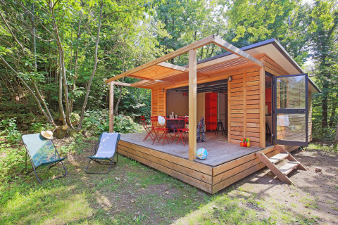Casetta in legno con terrazza e sedie da giardino immersa nel verde a Huttopia Royat, Alvernia-Rodano-Alpi, Francia.