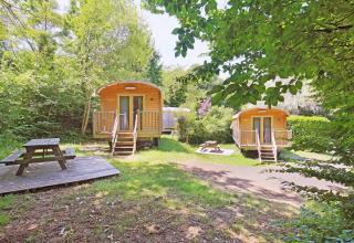 Twee houten hutten en picknickbanken in het groen op vakantiepark Huttopia Royat in Auvergne-Rhône-Alpes.