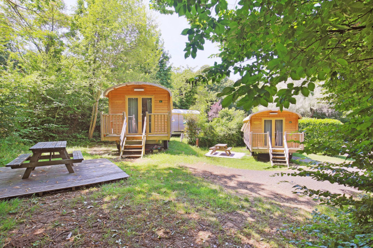 Zwei Holzhütten mit Picknicktischen in grüner Natur im Ferienpark Huttopia Royat in Auvergne-Rhône-Alpes.