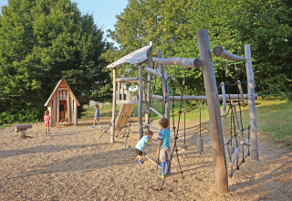 Children play on a wooden playground with climbing structures and playhouse at Huttopia Royat in France.