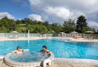 Buitenzwembad met jacuzzi en twee personen bij vakantiepark Huttopia Royat in Auvergne-Rhône-Alpes, Frankrijk.