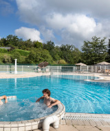 Piscina exterior con jacuzzi y dos personas en el parque vacacional Huttopia Royat, Auvernia-Ródano-Alpes, Francia.
