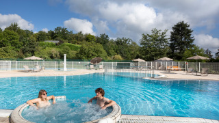 Piscina exterior con jacuzzi y dos personas en el parque vacacional Huttopia Royat, Auvernia-Ródano-Alpes, Francia.