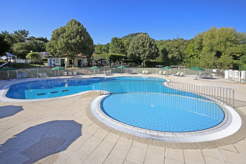 Piscina all'aperto presso Huttopia Royat, villaggio vacanze in Auvergne-Rhône-Alpes, Francia, circondata da alberi.