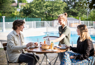 Un couple prend le petit-déjeuner en plein air près de la piscine au Huttopia Royat en Auvergne-Rhône-Alpes.
