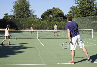 Vier mensen spelen tennis op een buitenveld bij vakantiepark Huttopia Royat, omringd door bomen in Frankrijk.