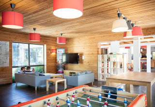 Gemeenschappelijke ruimte in Huttopia Royat met grijze zetels, tafelvoetbal en houten interieur.