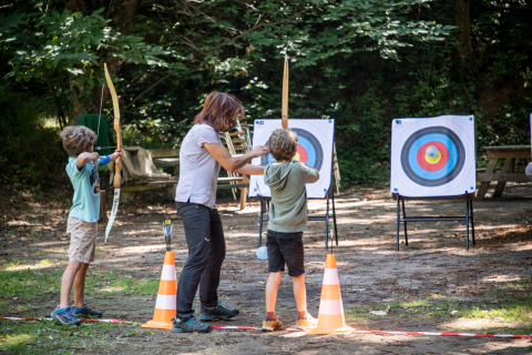 Niños aprenden tiro con arco con instructora al aire libre en Huttopia Royat, parque vacacional en Auvernia-Ródano-Alpes, Francia.