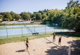 Vakantiepark met mensen bij beachvolleybal, tennisvelden en zwembad te Huttopia Royat in Frankrijk.