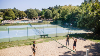 Parque vacacional con personas jugando voleibol de playa, canchas de tenis y piscina en Huttopia Royat, Francia.