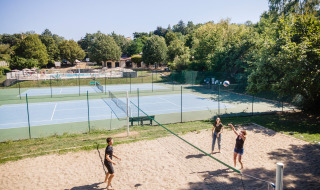 Parque vacacional con personas jugando voleibol de playa, canchas de tenis y piscina en Huttopia Royat, Francia.