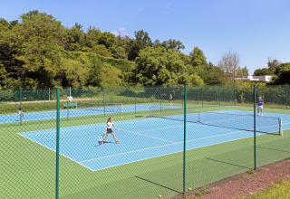 Kinderen en volwassenen spelen tennis op openluchtvelden omringd door groen in Huttopia Royat, Frankrijk.