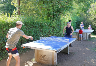 Mensen spelen buiten pingpong in vakantiepark Huttopia Royat, Auvergne-Rhône-Alpes, Frankrijk, temidden van groen.