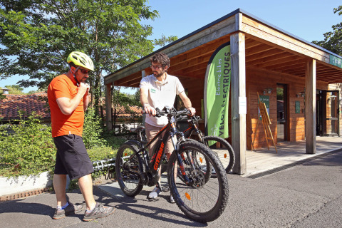 Dos hombres con bicicletas frente a una cabaña en Huttopia Royat, parque vacacional en Auvernia-Ródano-Alpes.
