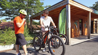 Dos hombres con bicicletas frente a una cabaña en Huttopia Royat, parque vacacional en Auvernia-Ródano-Alpes.