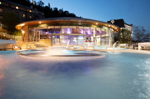 Piscina exterior climatizada en Huttopia Royat, parque vacacional de Auvernia-Ródano-Alpes, Francia, al anochecer.