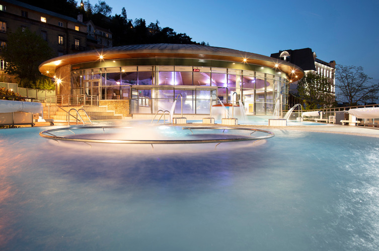 Beleuchtetes Außenschwimmbad von Huttopia Royat Ferienpark in Auvergne-Rhône-Alpes, Frankreich, bei Sonnenuntergang.