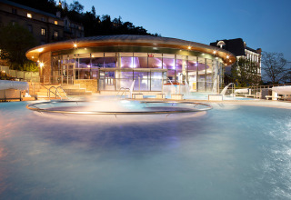 Verwarmd buitenzwembad van Huttopia Royat vakantiepark in Auvergne-Rhône-Alpes, Frankrijk, bij avondschemer.