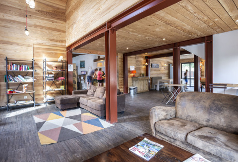 Sala luminosa con sofás, estantería y huéspedes en Huttopia Bourg Saint-Maurice, parque vacacional en Francia.