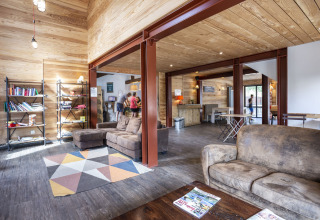 Helles Gemeinschaftszimmer mit Sofas, Bücherregal und Gästen im Huttopia Bourg Saint-Maurice, Frankreich.