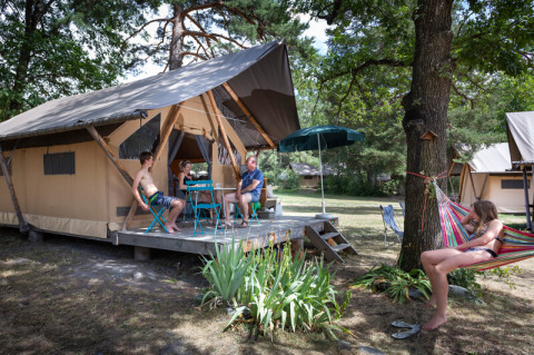 Familia relajándose fuera de su tienda en Huttopia Bourg Saint-Maurice, parque vacacional en Auvergne-Rhône-Alpes, Francia.