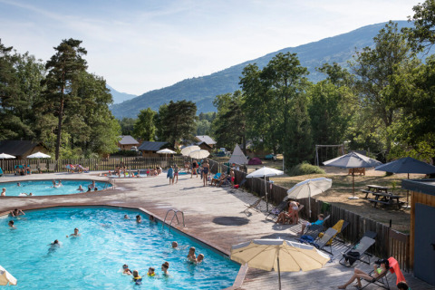 Piscina al aire libre en Huttopia Bourg Saint-Maurice con familias disfrutando de la naturaleza y las montañas.