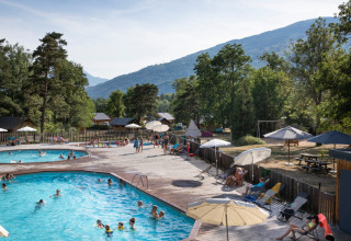 Piscine extérieure au Huttopia Bourg Saint-Maurice avec vacanciers, arbres et montagnes en arrière-plan.