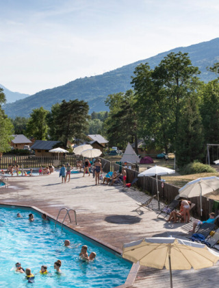 Piscina al aire libre en Huttopia Bourg Saint-Maurice con familias disfrutando de la naturaleza y las montañas.