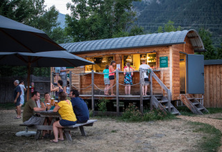 Bezoekers genieten aan een houten bar en picknickbank in Huttopia Bourg Saint-Maurice vakantiepark.