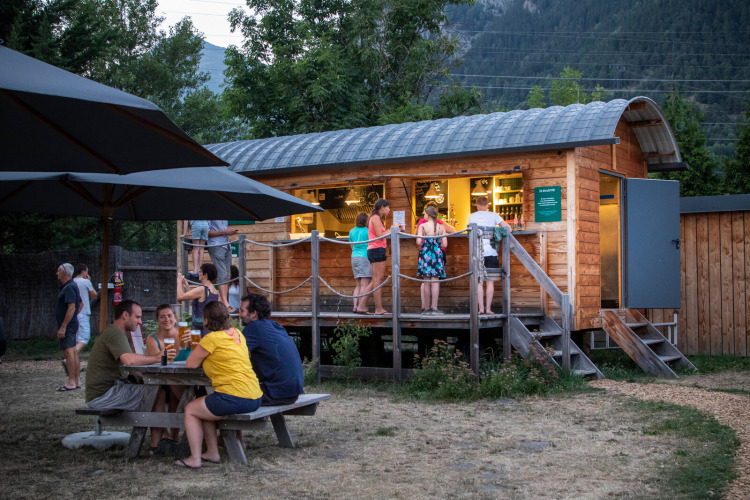 Gasten verzamelen zich bij een houten bar en picknicktafel in Huttopia Bourg Saint-Maurice vakantiepark.