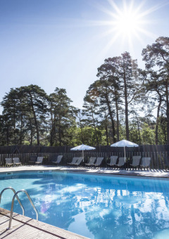 Piscina al aire libre en Huttopia Bourg Saint-Maurice, con montañas y árboles al fondo en un día soleado.