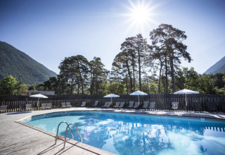 Piscine extérieure à Huttopia Bourg Saint-Maurice, entourée de montagnes et d’arbres, sous un soleil éclatant.