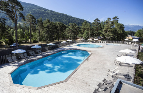 Outdoor swimming pool with deck chairs and parasols, set among pines and mountains at Huttopia Bourg Saint-Maurice.