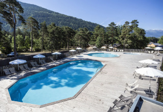 Piscine extérieure entourée de transats et de parasols, au cœur des pins et montagnes à Huttopia Bourg Saint-Maurice.