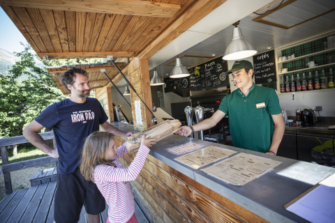 Een meisje en een man nemen pizza aan een buitenbalie op Huttopia Bourg Saint-Maurice in Frankrijk.