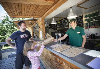 Een meisje en een man nemen pizza aan een buitenbalie op Huttopia Bourg Saint-Maurice in Frankrijk.