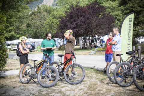Personas conversan junto a bicicletas eléctricas en Huttopia Bourg Saint-Maurice, parque vacacional en Francia.