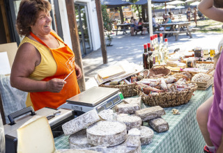 Vriendelijke vrouw in oranje schort verkoopt kaas en charcuterie op de markt van Huttopia Bourg Saint-Maurice, Frankrijk.