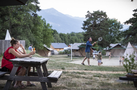 Parque vacacional Huttopia Bourg Saint-Maurice en Francia con personas relajándose y jugando bádminton afuera.