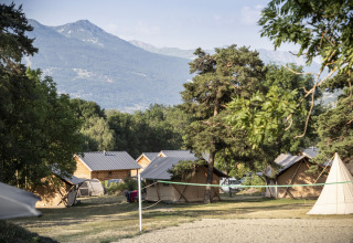 Hutten en tenten tussen bomen met bergen op de achtergrond bij Huttopia Bourg Saint-Maurice in Frankrijk.