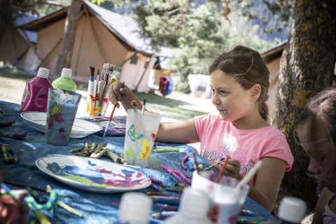 Una bambina dipinge artigianato all'aperto su un tavolo a Huttopia Bourg Saint-Maurice, Auvergne-Rhône-Alpes.